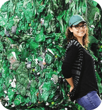 Woman leaning against a bail of green recycled plastic.